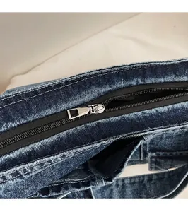 Detailed close-up of smooth silver metal zipper on washed blue denim fabric bag