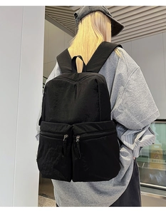 Rear view of model wearing minimalist black nylon travel backpack with dual front pockets