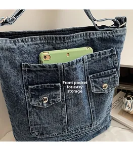 Detail of blue denim tote bag featuring front utility pockets for smartphone storage