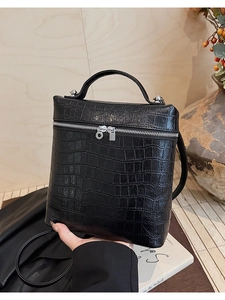 Detail of black crocodile-embossed handbag with silver zippers and single top handle
