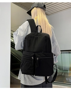 Rear view of a large black nylon travel backpack worn in a modern outdoor urban setting