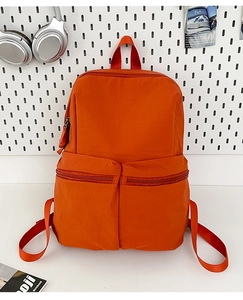 Detail view of orange nylon backpack with dual front zippers on white pegboard