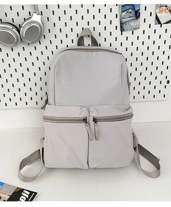 Close-up of a light grey water-resistant backpack with dual front zipper pockets and top handle