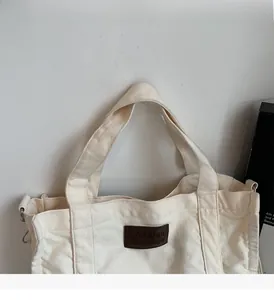 Detail of white canvas tote bag featuring brown leather tag and silver metal rings