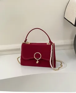 Close-up of red bridal handbag with gold ring clasp and elegant pearl chain detail