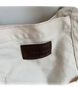 Detail of off-white canvas tote with a brown leather patch debossed with Fashion Luggage