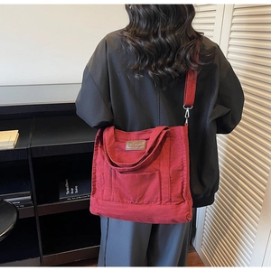 Detail of red canvas tote bag featuring leather logo patch and silver metal hooks