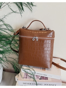 Detail of a brown crocodile pattern square bag with dual silver zippers and top handle