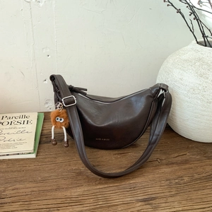 Détail du sac demi-lune marron foncé avec logo doré et breloque peluche sur bois