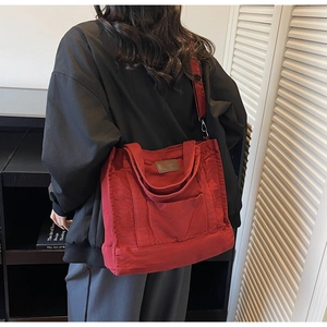 Detailed side view of deep red canvas tote bag worn by a model in a minimalist room