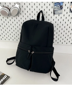 Detail of minimalist black nylon backpack featuring multi-zipper front pockets and waterproof fabric