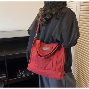 Deep red canvas tote bag with brown leather label worn on shoulder in a stylish setting