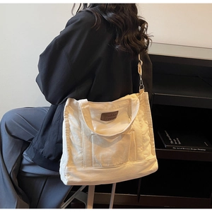 Detail of cream canvas tote bag with brown leather label and adjustable shoulder strap