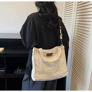 Detail of a large cream canvas tote bag with brown leather patch and adjustable strap