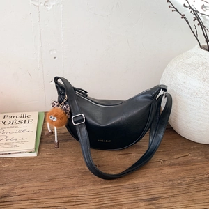 Détail d'un sac demi-lune noir avec logo doré et charmant pendentif en peluche doux
