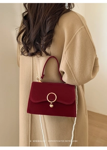 Detail of red velvet handbag featuring golden ring clasp and elegant pearl chain strap