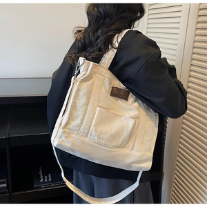 Detailed shot of an off-white canvas tote bag with a leather tag and adjustable strap