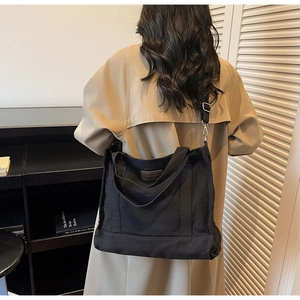 Detail view of large black canvas tote bag with adjustable nylon strap and logo leather patch