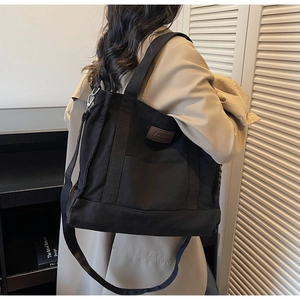 Detail of a black large capacity canvas tote bag with adjustable strap and leather patch