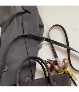 Detail of adjustable leather shoulder strap and cute bear pendant on brown handbag