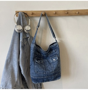 Detail of blue washed denim tote bag showing functional front flap pockets and metal buttons