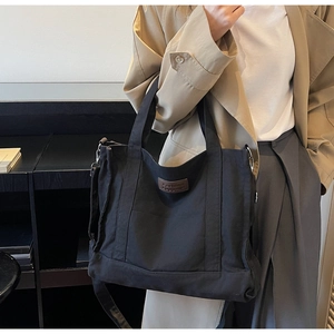 Detail of black canvas tote bag with brown leather label and adjustable shoulder strap