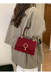 Detail of red velvet handbag featuring pearl chain and gold metal buckle on trench coat