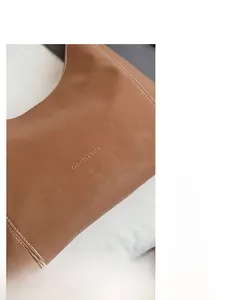 Detailed close-up of brown pebbled leather tote bag with white stitching and embossed logo