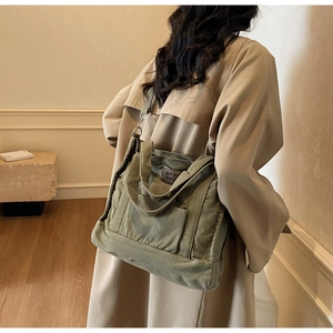 Close-up of a dark green canvas tote bag with brown leather label on a trench coat