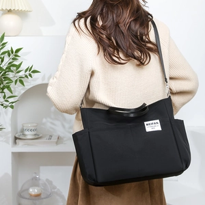 Detail of black nylon multi-pocket tote bag with white fashion label on minimalist model