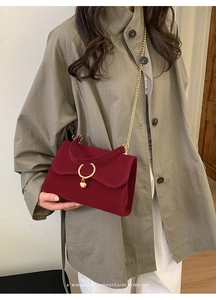 Detail of red velvet crossbody bag with golden heart lock and chain strap on model
