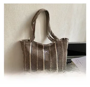 Close-up of brown striped canvas tote bag with bow detail and large laptop capacity