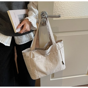 Detail einer cremefarbenen Canvas-Tragetasche mit Vordertaschen an einem Türgriff