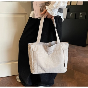 Detailansicht der beigen Tragetasche mit aufgesetzter Tasche und kleinem gewebten Etikett