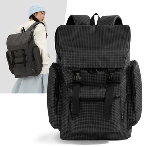 Detail view of plaid backpack featuring dual buckle straps and large front zip pocket