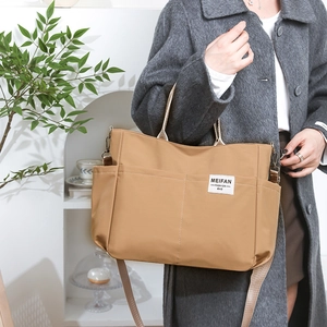 Detail of khaki nylon tote bag showing durable side pockets and woven label on a person