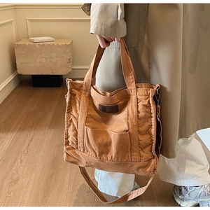 Detail of brown canvas tote bag with leather logo tag and shoulder strap on model