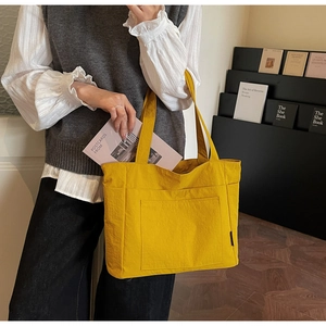 Gelbe Nylon-Tragetasche mit großer Vordertasche und minimalistischem Logo im Detail
