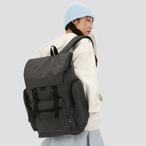 Detailed view of black checkered backpack showing side zipper pocket and flap buckle closure