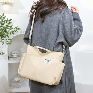 Close-up of beige nylon tote bag with side pockets and adjustable shoulder strap worn by model