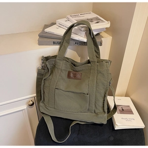 Close-up of military green canvas tote bag with adjustable strap and leather logo tag