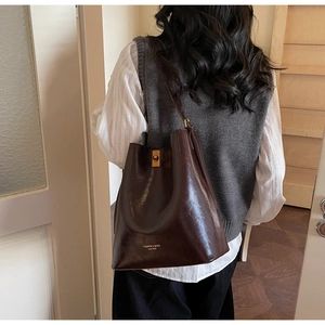 Close-up of deep brown glossy bucket bag with golden twist lock and printed leather text