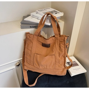 Detail of tan canvas tote bag featuring brown faux leather label and front pocket