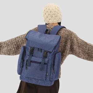 Detail of navy blue plaid backpack with adjustable straps and side brand label shown on back