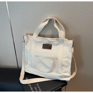 Detail view of large canvas tote bag with brown leather logo patch and front pocket