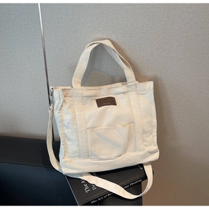 Detailed view of cream canvas tote bag with brown leather patch and adjustable strap