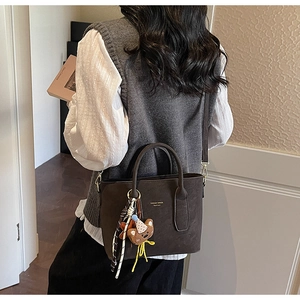 Detail of a dark brown suede bucket bag featuring a bear charm and elegant brand logo