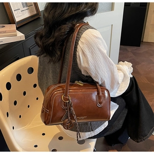 Sac polochon vintage en cuir marron brillant avec pendentif porté par un mannequin