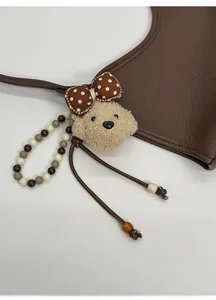 Détail d'un bijou de sac caniche en peluche avec cordon perlé sur sac en cuir marron