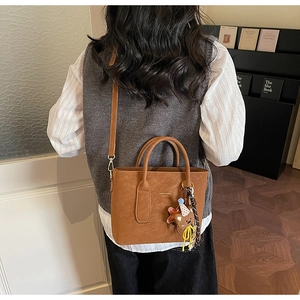 Detail of brown matte leather tote bag with gold logo, teddy charm and silk scarf